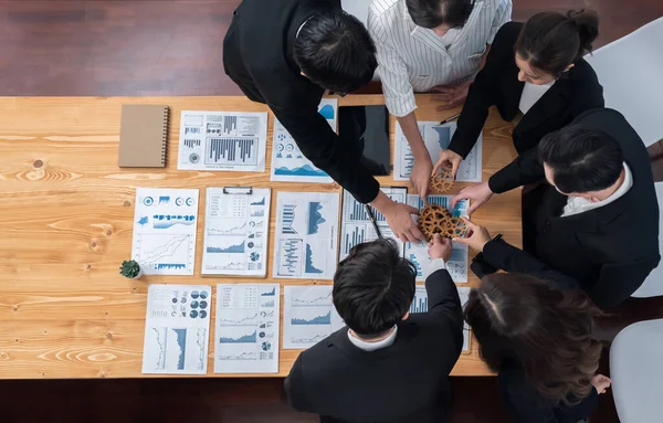 Top view hand holding gear by businesspeople wearing suit for harmony synergy in office workplace concept. Group of people hand making chain of gears into collective form with dashboard report papers.