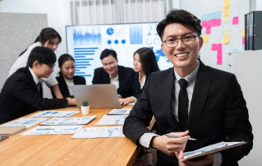 Focus portrait of successful confident male manager or executive in business wear with blurred background of businesspeople, colleagues working with financial report papers in office of harmony.