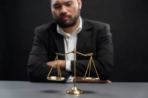 Focus golden scale balance with burred background of lawyer in black suit sit on his office desk, symbol of legal justice and integrity, balanced and ethical decision in court of law equility