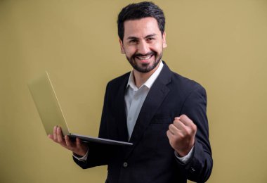 Yenilikçi teknoloji kavramına sahip başarılı bir iş adamı, ayakta duran, dizüstü bilgisayarı tutan ve telif alanı arka planında reklam ya da tanıtım için heyecanla gülümseyen. Coşkulu