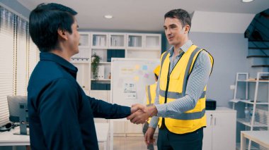 An engineer with a protective vest handshake with an investor in his office. Following a successful meeting, employee and employer form a partnership.