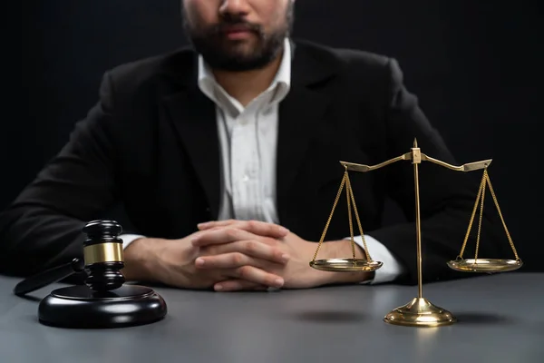 Focus symbols of justice, gavel hammer and scale balance on blurred background of thoughtful lawyer or judge sitting at his desk for integrity and fairness of the legal system. equility