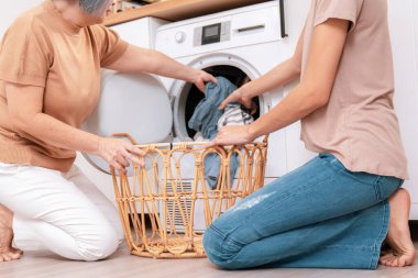 Daughter and mother working together to complete their household chores near the washing machine in a happy and contented manner. Mother and daughter doing the usual tasks in the house.