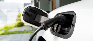 Closeup electric vehicle plugged-in with cable from charging point powered for progressive concept by alternative clean energy rechargeable EV car at home charging station.
