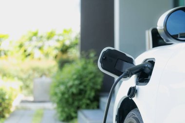 Closeup electric vehicle plugged-in with cable from charging point powered for progressive concept by alternative clean energy rechargeable EV car at home charging station.