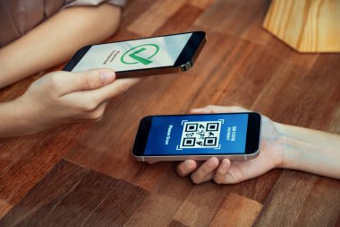 QR kodu parasız ödeme taraması için ekranda gösterilir. Kapalı eller, mobil uygulamadan elektronik işlem yoluyla para aktarmak için akıllı telefonu tutuyor. Hızlı ödeme için barkod teknolojisi. Coşkulu.
