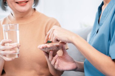 Contented senior woman taking medicines while her caregiver advising her medication. Medication for seniors, nursing house, healthcare at home.