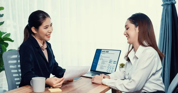 Two asian women conduct job interview in office. Applicants wear formal suit while talking about her CV and job application. Interviewer ask inquiry in positive and conversational manner. Enthusiastic