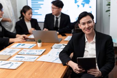 Focus portrait of successful confident male manager or executive in business wear with blurred background of businesspeople, colleagues working with financial report papers in office of harmony.