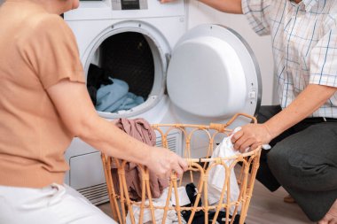 Senior couple working together to complete their household chores at the washing machine in a happy and contented manner. Husband and wife doing the usual tasks in the house.