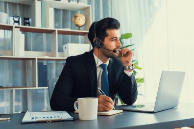 Erkek çağrı merkezi operatörü ya da telesales temsilcisi ofis masasında oturmuş kulaklık takıyor ve müşteri hizmetleri desteği sağlayan ya da satış yapan müşteriyle sohbet ediyor. coşkulu