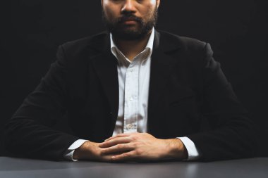 Resmi siyah takım elbiseli bir iş adamı ya da avukat izole edilmiş siyah arka planda oturuyor. Otorite ve ciddi jestleri olan bir adam kavramı. denge