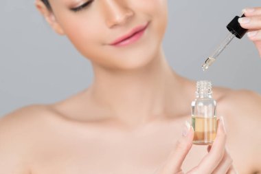 Focus cannabis extracted oil bottle with dropper lid holding by blurred glamorous beautiful asian woman with perfect clean skin and soft smooth makeup in isolated background.