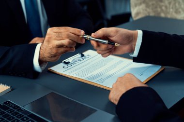 İş anlaşması yapılırken iki işadamı masanın karşısında oturuyor. Şirket avukatı, sözleşmeyi imzalaması için müvekkiline ya da ortağına kalem veriyor ve anlaşmayı imzayla imzalıyor. Coşkulu