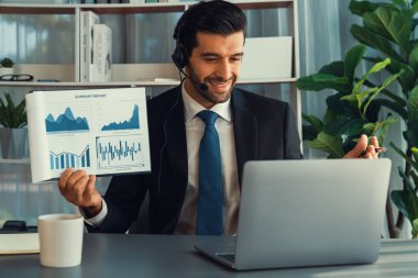 Kulaklık takan bir iş adamı online toplantı sırasında bilgisayarla finansal veri ya da BI kağıdı sunar. Etkili uzaktan çalışmanın sanal toplantı sunumuyla uzaktan çalışma konsepti. Coşkulu