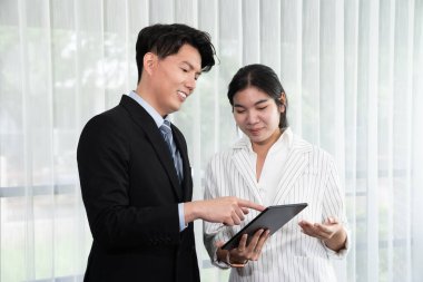 Manager advising guiding younger colleague with tablet in workplace. Couple businesspeople in formal wear working together on financial strategy as concept of teamwork and harmony in office.