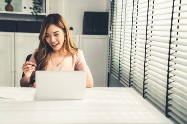 A young Asian female employee sitting at her desk in her office, sitting at desktop in workstation.