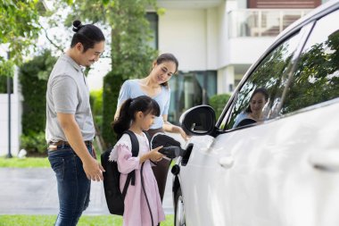 Progressive young happy family with electric vehicle and home backyard charging station. Green and clean energy from electric vehicles for healthy environment. Eco power from renewable source.