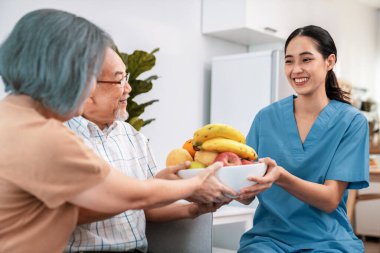 Contented senior couple taking a bowl of fruit from a nurse at home. Senior care at home.
