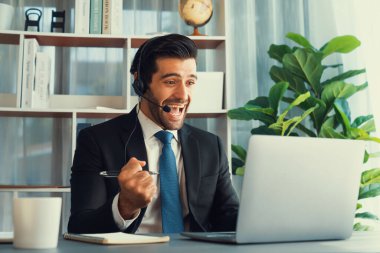 Siyah takım elbiseli heyecanlı ve mutlu iş adamı, ofis masasında kutlama jesti olarak kolunu kaldırdı. İş yerinde başarılı bir çağrı merkezi ya da telesales operatörü kutlama yapıyor. Coşkulu