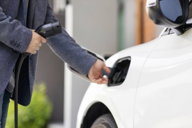 Closeup progressive asian man install cable plug to his electric car with home charging station. Concept of the use of electric vehicles in a progressive lifestyle contributes to clean environment.