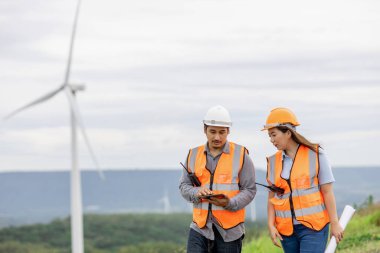 Erkek ve kadın mühendisler kırsal kesimdeki bir tepenin tepesinde ya da dağda rüzgar çiftliğinde çalışıyorlar. Yenilenebilir ve sürdürülebilir enerjinin gelecekteki üretimi için yenilikçi idealler.