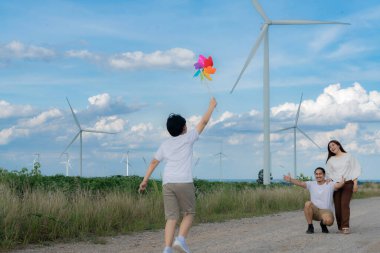 Progressive happy family enjoying their time at wind farm for green energy production concept. Wind turbine generators provide clean renewable energy for eco-friendly purposes.