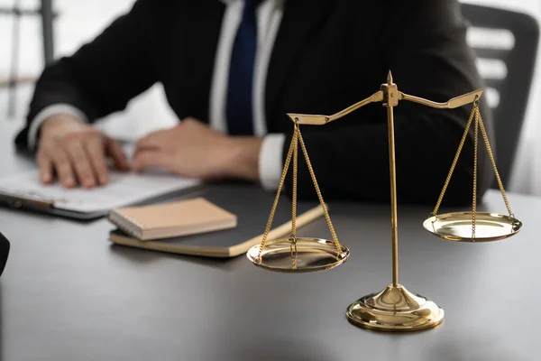 Focus shiny golden balanced scale on blurred background of lawyer working in his desk at law firm office. Scale balance for righteous and equality judgment by lawmaker and attorney. Equilibrium