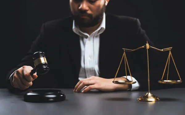Focus symbols of justice, gavel hammer and scale balance on blurred background of thoughtful lawyer or judge sitting at his desk for integrity and fairness of the legal system. equility
