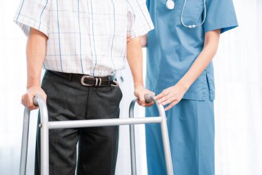 Physiotherapist assists her contented senior patient on folding walker. Recuperation for elderly, seniors care, nursing home.