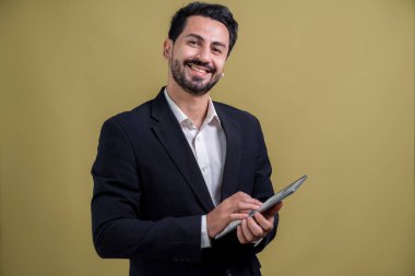 Resmi takım elbiseli kendine güvenen işadamı elinde tabletle sürpriz bir şekilde terfi ya da reklam arıyor. Yüz ifadeleri ve jestler, izole bir arkaplanda heyecan ve şaşkınlığa işaret ediyor. Coşkulu