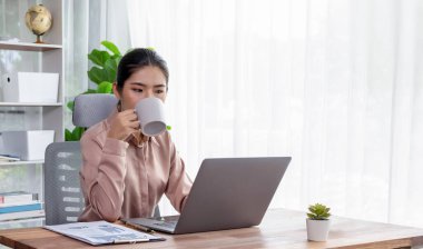 Modern ofis masasındaki Asyalı hevesli genç iş kadını çalışmak ve notlar yazmak için dizüstü bilgisayar kullanıyor. Çalışkan ve çekici ofis hanımı ofisinde bilgisayar defteri üzerinde çalışıyor..