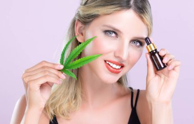 Mükemmel makyajlı güzel bir kadının çekici portresi yeşil yaprak, cilt bakımı ürünü için marihuana özlü şişe. Kozmetik ve güzellik için pembe izole edilmiş arka planda esrar CBD yağı