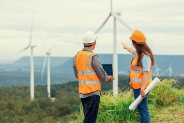 Erkek ve kadın mühendisler kırsal kesimdeki bir tepenin tepesinde ya da dağda rüzgar çiftliğinde çalışıyorlar. Yenilenebilir ve sürdürülebilir enerjinin gelecekteki üretimi için yenilikçi idealler.