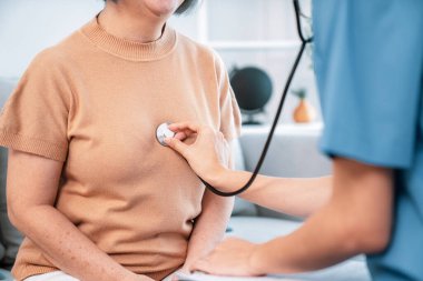 A contented retired senior woman being exterminated by her caregiver with a stethoscope at home. Medical care service, senior care at home.