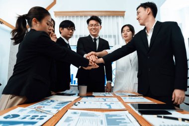 Closeup business team of suit-clad businessmen and women join hand stack together and form circle. Colleague collaborate and work together to promote harmony and teamwork concept in office workplace.