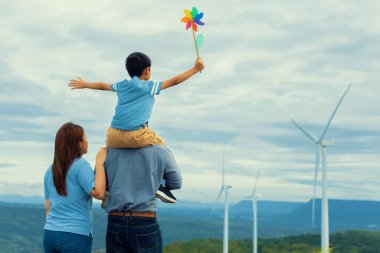 Progressive happy family enjoying their time at wind farm for green energy production concept. Wind turbine generators provide clean renewable energy for eco-friendly purposes.