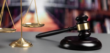 Adalet ve hukuki otorite kavramının simgesi olarak mahkeme kütüphanesinde parlak altın dengeli ölçek ve ahşap tokmak avukat ve yargıç tarafından eşitlik ve adil yargılamayı yansıtıyor. denge