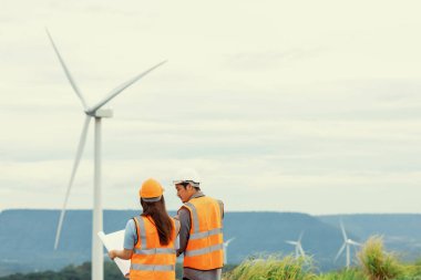 Erkek ve kadın mühendisler kırsal kesimdeki bir tepenin tepesinde ya da dağda rüzgar çiftliğinde çalışıyorlar. Yenilenebilir ve sürdürülebilir enerjinin gelecekteki üretimi için yenilikçi idealler.