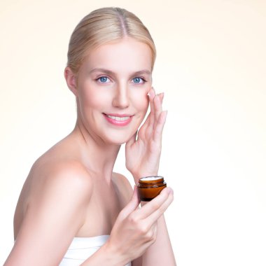 Closeup personable beautiful perfect clean skin soft makeup woman finger applying moisturizer cream on her face for anti aging wrinkle. Facial rejuvenation with expressive hand gesture putting cream.