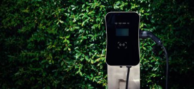 Charging station with greenery foliage background for combination of nature and alternative energy for progressive future renewable energy for electric car. Charger point with connecter device.
