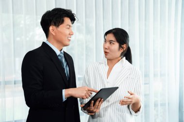 Manager advising guiding younger colleague with tablet in workplace. Couple businesspeople in formal wear working together on financial strategy as concept of teamwork and harmony in office.