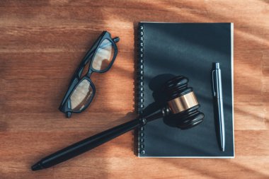 Yakın plan siyah tahta tokmak çekiç ile ahşap ofis masası arka planında kitap ve gözlükler avukat ve hakim için adalet sistemi olarak, mahkemelerde otoriteyi ve adaleti sembolize eder. denge