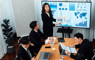 Confidence and young asian businesswoman give presentation on financial business strategy in dashboard report display on screen to colleagues in conference room meeting as harmony in workplace concept
