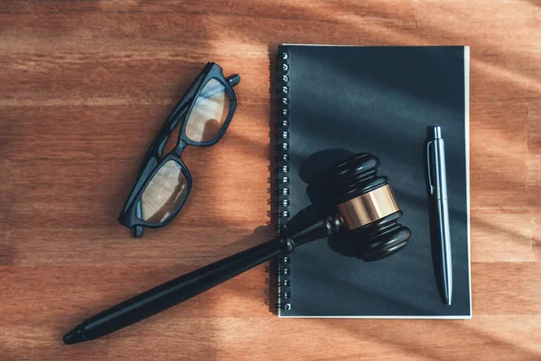 stock image Closeup top view black wooden gavel hammer with book and glasses on wooden office desk background as justice legal system for lawyer and judge, Symbolize authority and fairness in trials. equility