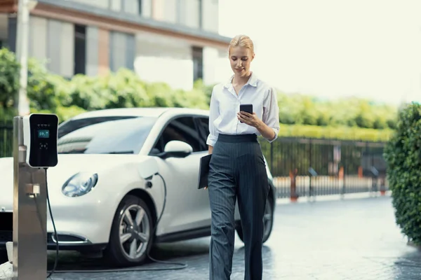 Businesswoman Using Tablet Walking While Recharging Her Electric Vehicle Charging — 图库照片