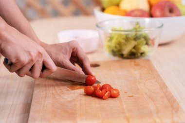 Close up hands holding a knife preparing a contented meal. Sliced tomatoes and other vegetables on the glass dish.