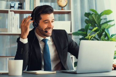 Siyah takım elbiseli heyecanlı ve mutlu iş adamı, ofis masasında kutlama jesti olarak kolunu kaldırdı. İş yerinde başarılı bir çağrı merkezi ya da telesales operatörü kutlama yapıyor. Coşkulu