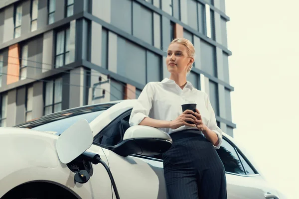 Businesswoman Drinking Coffee Leaning Electric Vehicle Recharging Public Charging Station — Photo