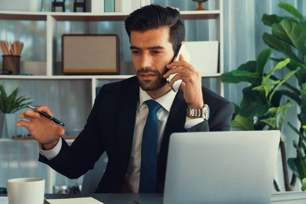 Çalışkan işadamı, ofisindeki dizüstü bilgisayarla cep telefonlu, modern, çalışkan ofis çalışanı yaşam biçimi konsepti olarak çalışırken müşterileriyle telefonda konuşmakla meşgul. Coşkulu